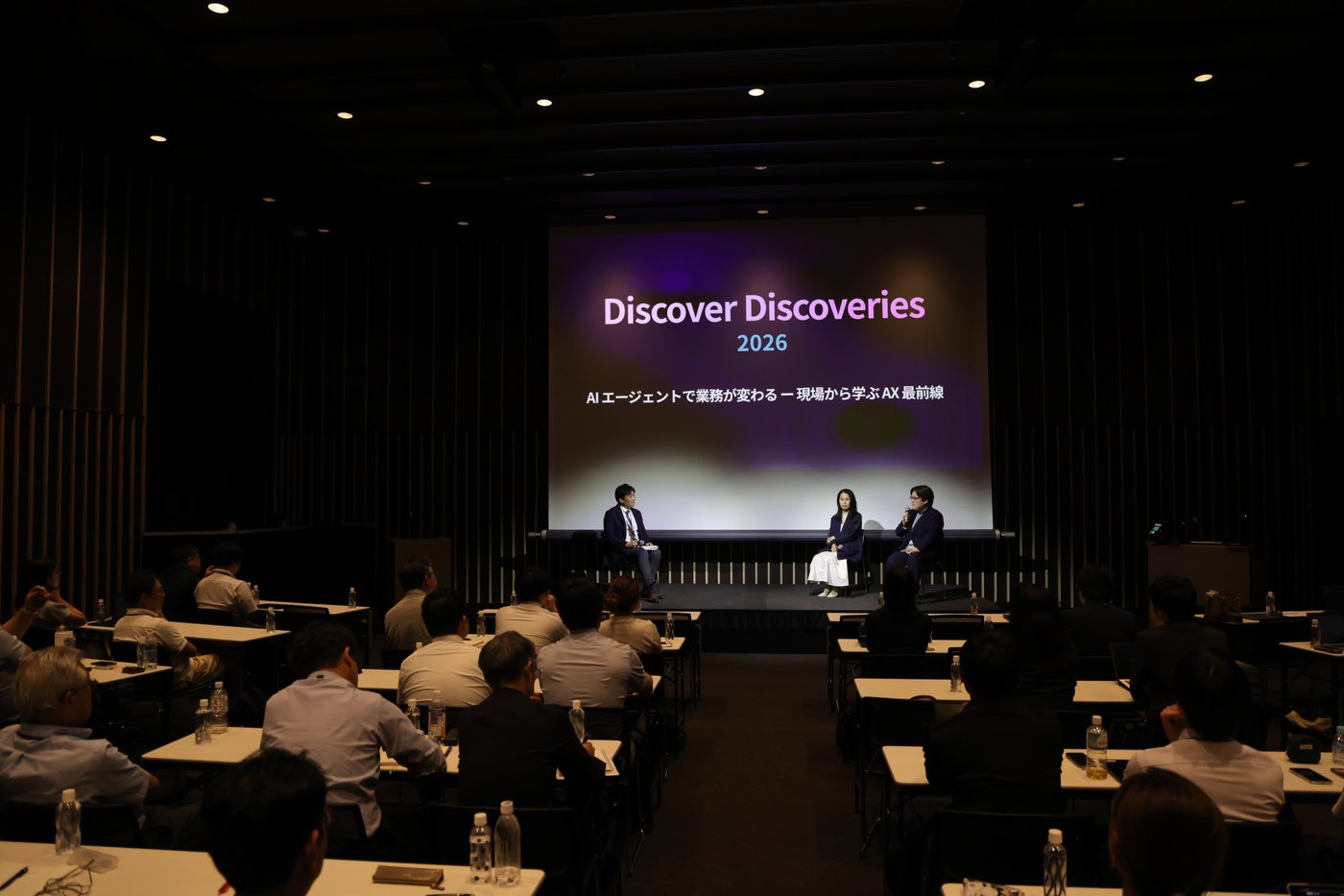 パネルディスカッションの様子。登壇者 3 名がステージ上で対話し、会場の参加者が着席して聞いている